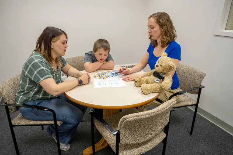 A little boy and his mom sits at a table with Katie Edler discussing their session.