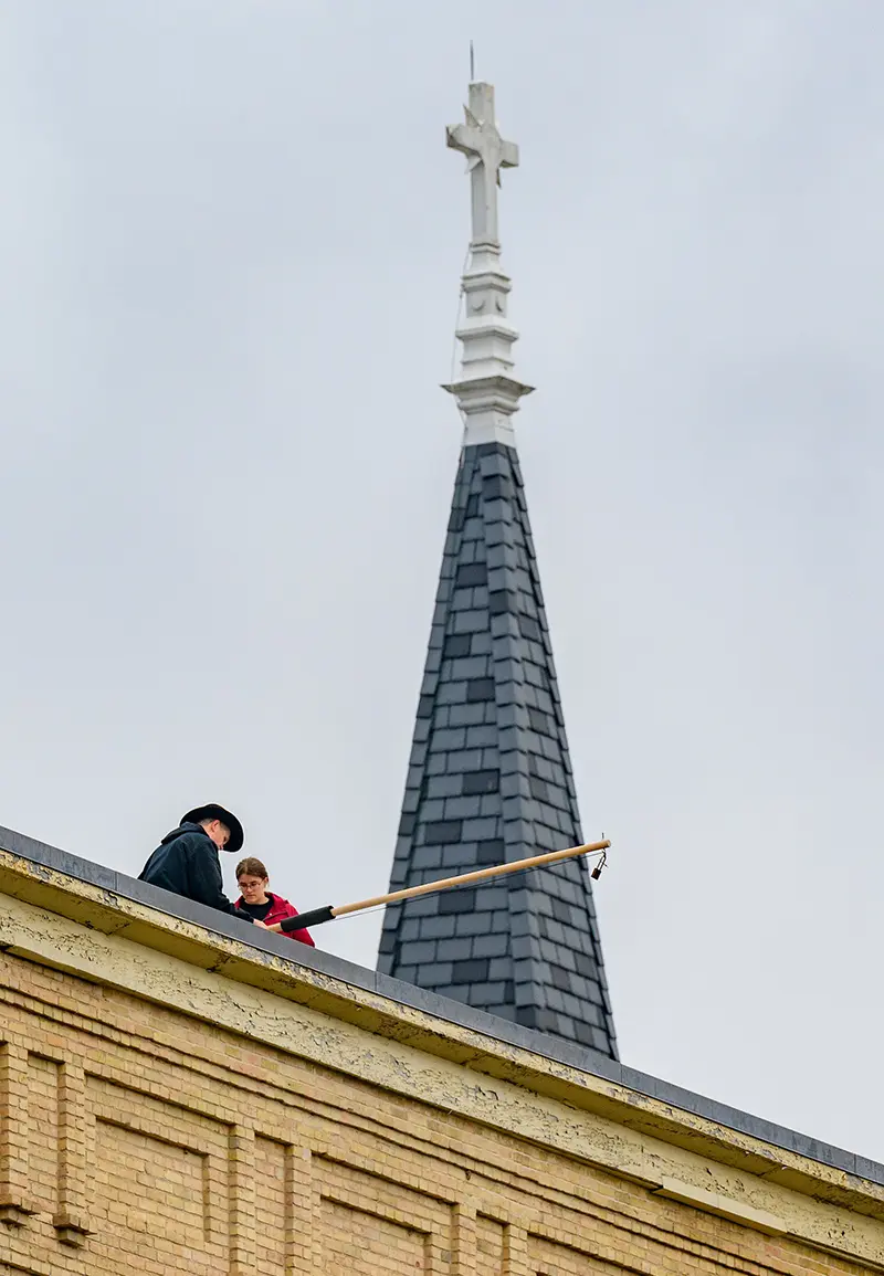 Team working on the roof of Bertrand Hall to install a rod that is used to hang the wire needed for the experiment.