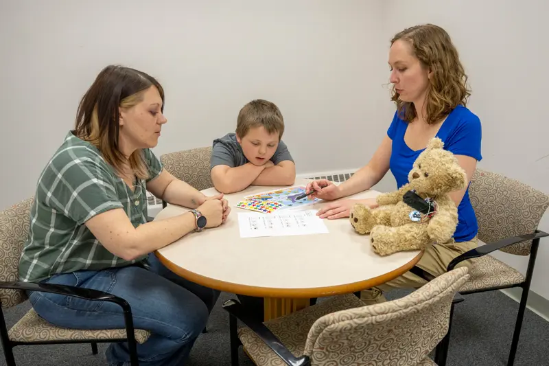 A little boy and his mom sits at a table with Katie Edler discussing their session.