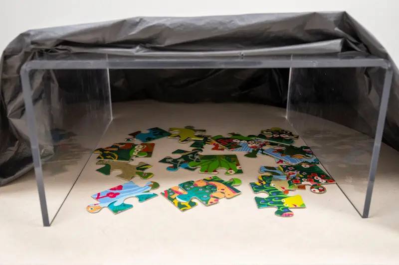 A puzzle under a clear stand that's partially covered with a black cloth.