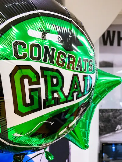 A metallic green and black graduation balloon with “CONGRATS GRAD” and a diploma illustration on it.