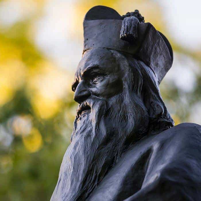 Close-up on the face of a statue of Rev. Edward Sorin. He has a long full beard and is wearing a tall hat.