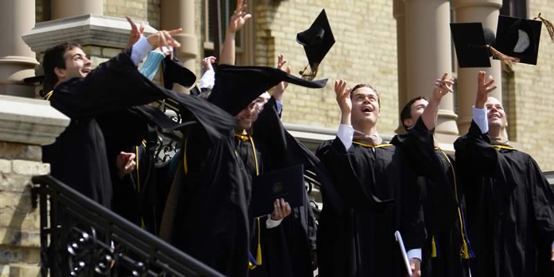 Male students wearing black robes and tossing their caps on the steps of the Main Building