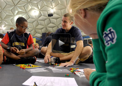 Two Notre Dame students and a fifth-grade boy working with Legos on the floor