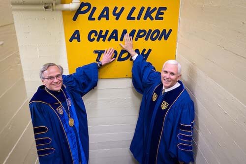 University of Notre Dame President Rev. John I. Jenkins, C.S.C. and Vice President Mike Pence touch the 'Play Like a Champion Today' sign in the football locker room before Commencement 2017.
