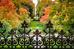 A close up shot of a fence with colorful fall trees in the background.