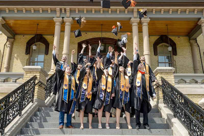 Graduates toss their caps in the air on the steps of the Main Building.