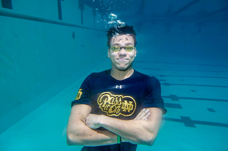 A college student wearing goggles crosses his arms and floats under water.