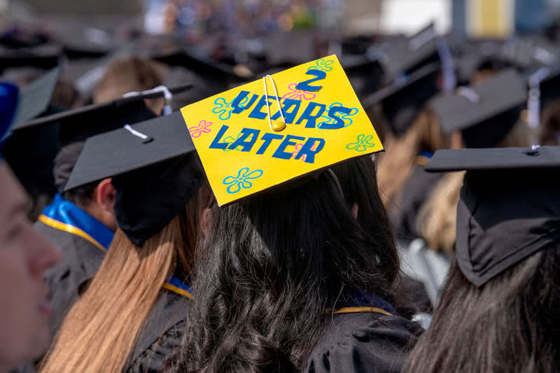 Graduation ceremony with the student facing away showing the top of the cap that reads '2 years later'