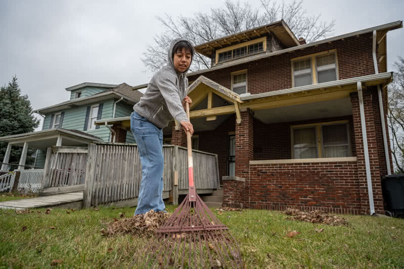 Student raking leaves in front of a home with a wooden ramp.