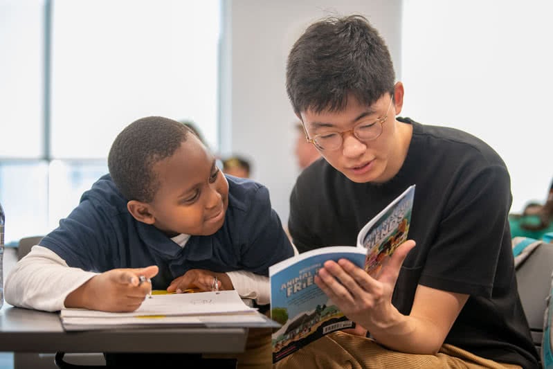 Older student assisting a younger student with an activity book.