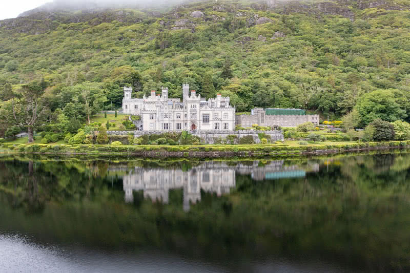 Aerial photo of Kylemore Abbey at the base of a foggy mountain with reflection on the lake.