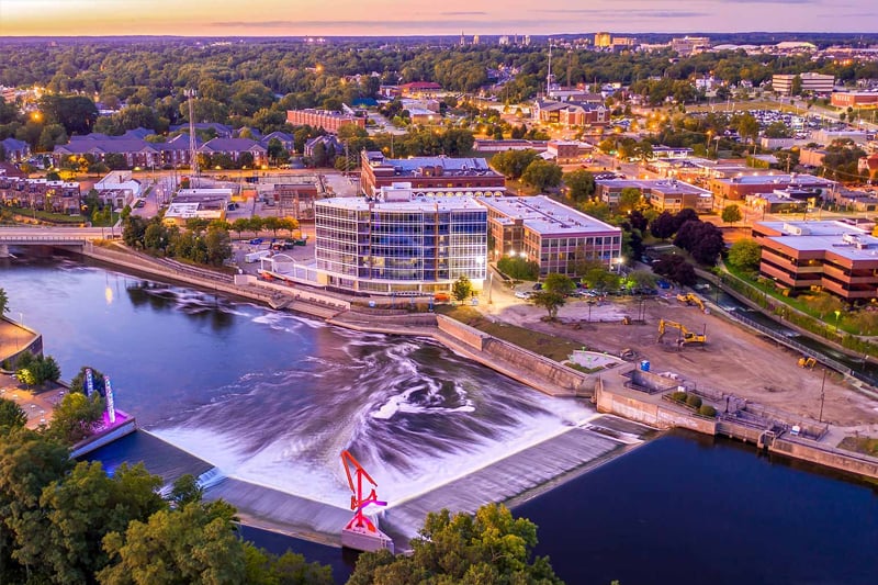 A nighttime photo of downtown South Bend along the St. Joseph River dam. Lights in the city are glowing yellow.