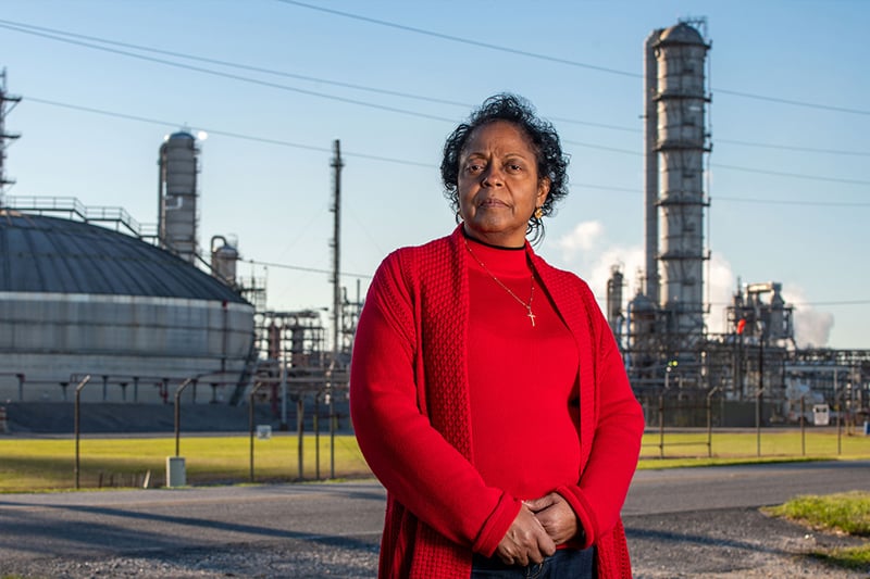 Photo of Sharon Lavigne standing in the foreground with out of focus industrial buildings in the background.