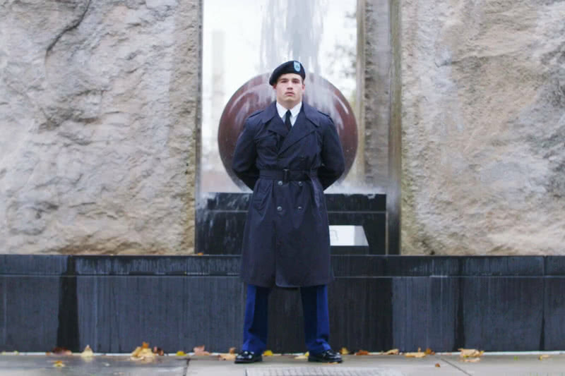 Member of the ROTC stands at salute in front of the Clarke Memorial on campus