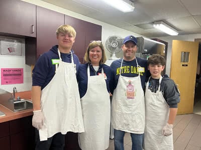 Four people in aprons stand in a kitchen.