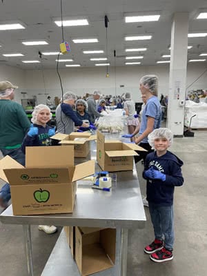 A large group of people in a kitchen load boxes with food.