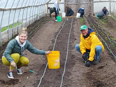 Two people plant seeds in a greenhouse.