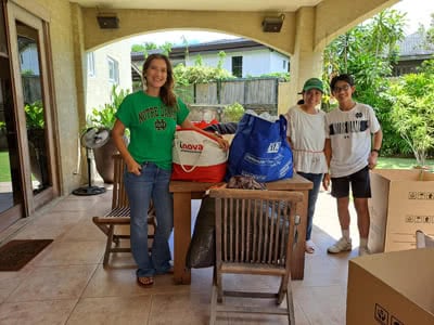 A group of three stand by a patio table with bags of clothing on it.