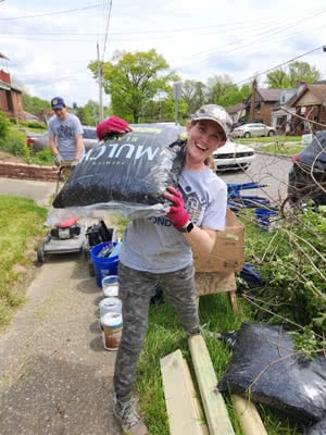 A woman carries a bag of mulch.