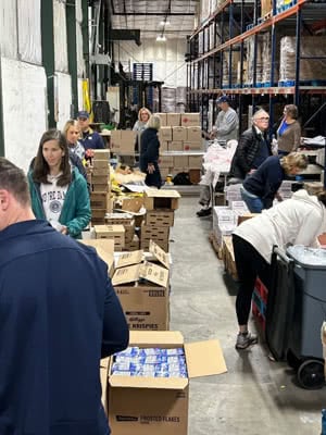 A group of people in a warehouse pack boxes of food.