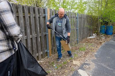 A man pick up trash with a pole grabber in a backyard.