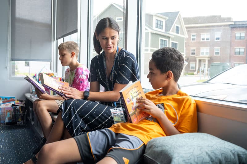 A Notre Dame students reads with two young kids on a window bench. 