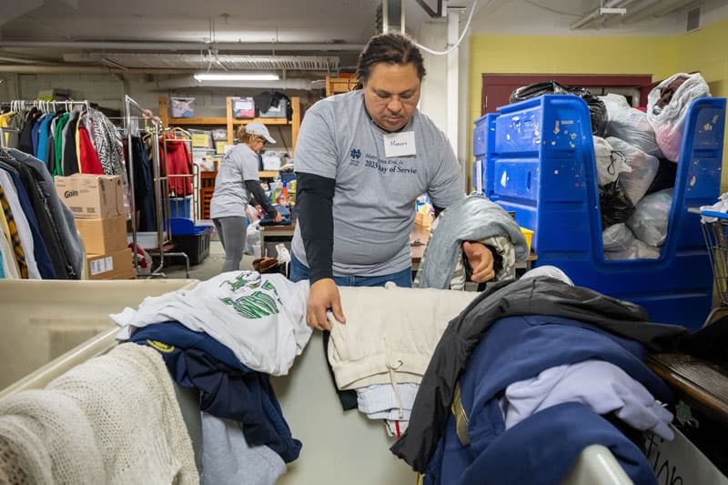 A man stands in front of a laundry bin folding clothes.