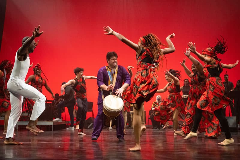 A group of UZIMA dancers on a stage under red lights.