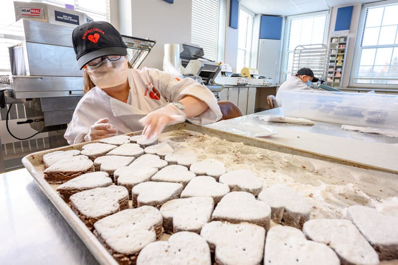 A person in front of a baking tray full of heart shaped treats.