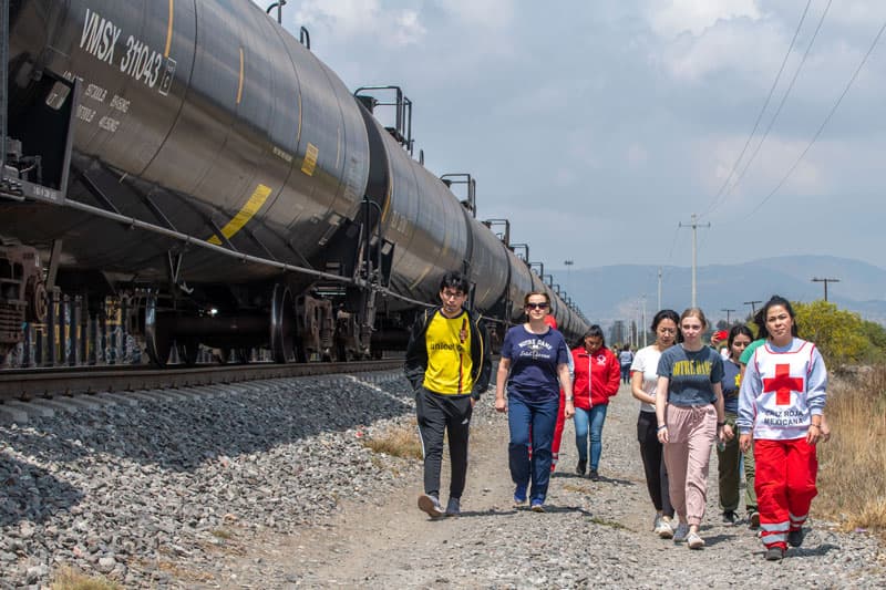 A group of people, including a Red Cross worker, walk next to a train in Puebla, Mexico.