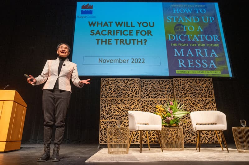 Maria Ressa stands on stage giving a lecture.