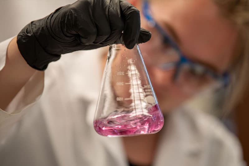 A close up of a beaker with pink liquid in it.