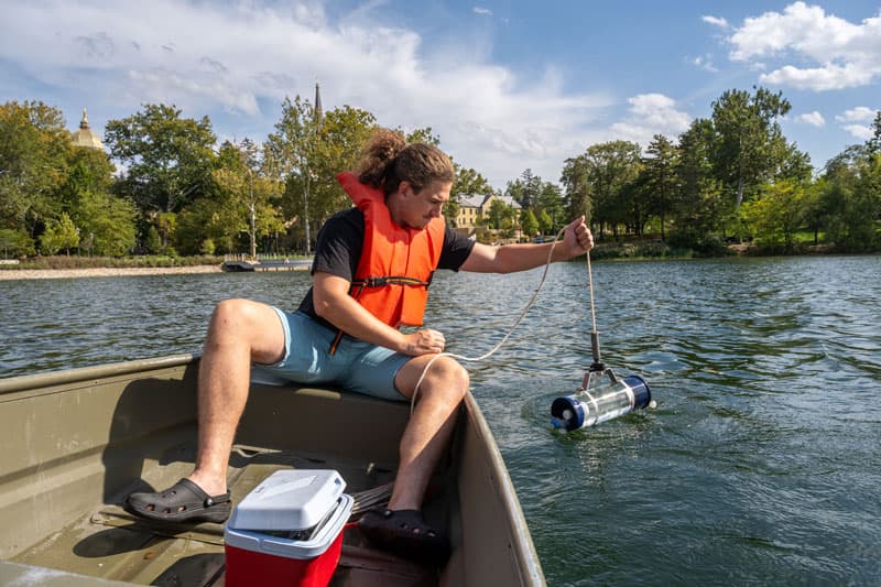 A students sits in a canoe on Saint Mary's Lake putting a water collection device into the water.