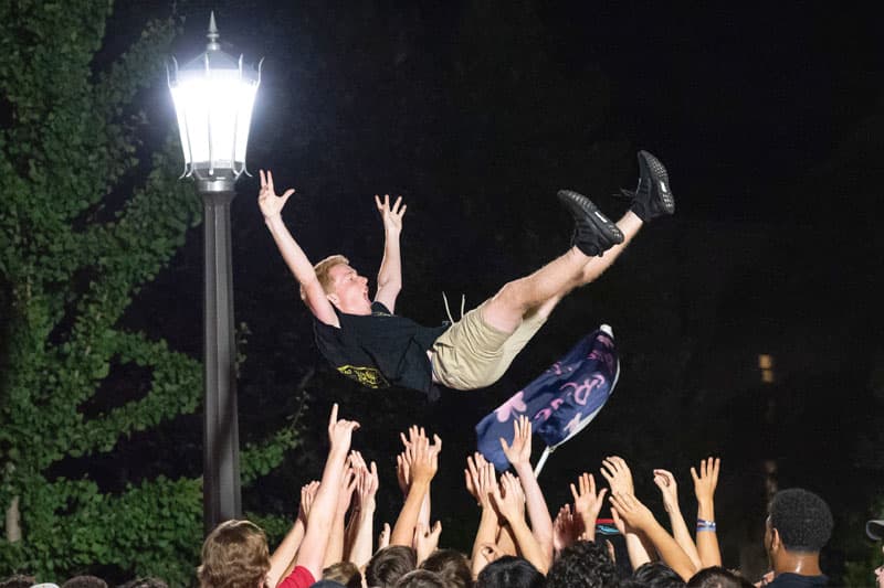 A bunch of hands throwing a male into the air.