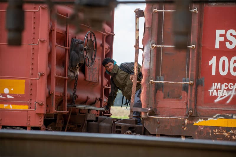 A man riding a train in motion looking off frame in a seemingly perilous situation.