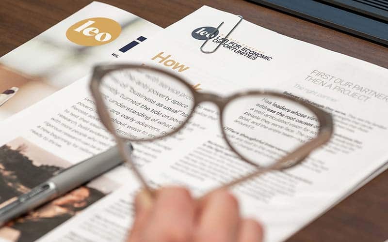 Papers and booklets on a desk and glasses in blurred in the foreground.