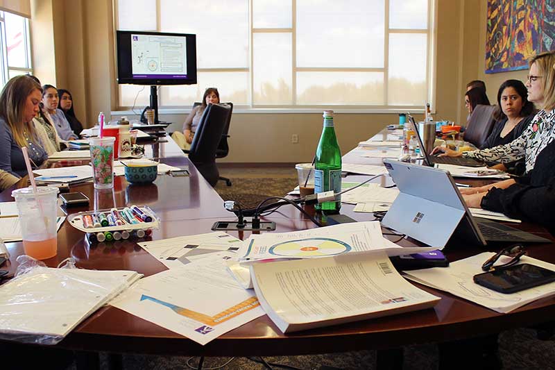 A team meets around a conference table covered in books and papers.