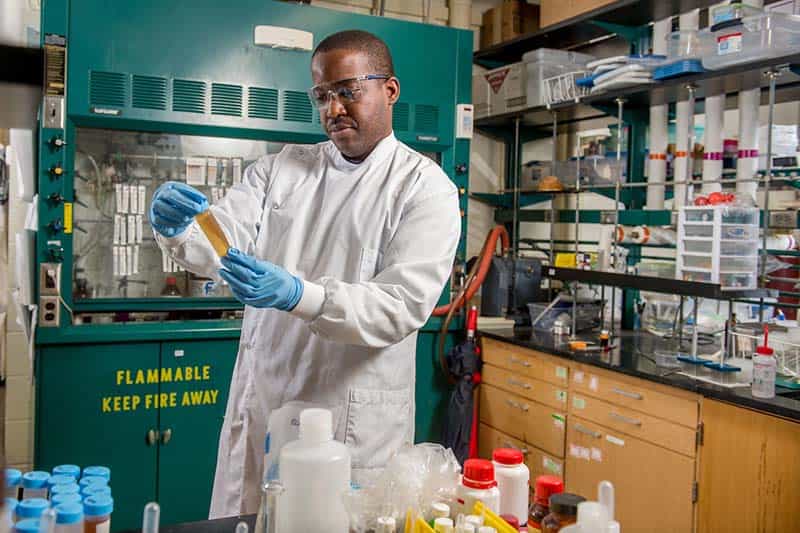 A male in a lab coat holds a sample.