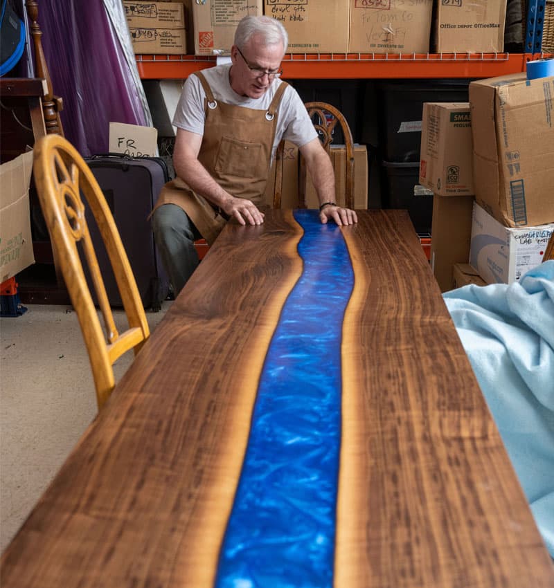 Fr. Groody sitting down next to his newly completed river table.