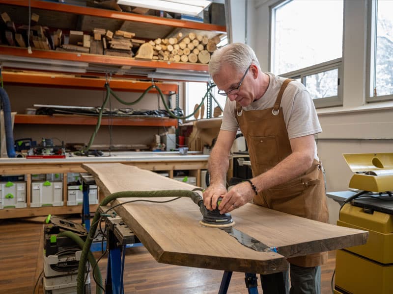 Fr. Dan Groody works on the table with a hand sander.