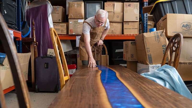 In his workshop, Fr. Groody stands inspecting the river table he made.