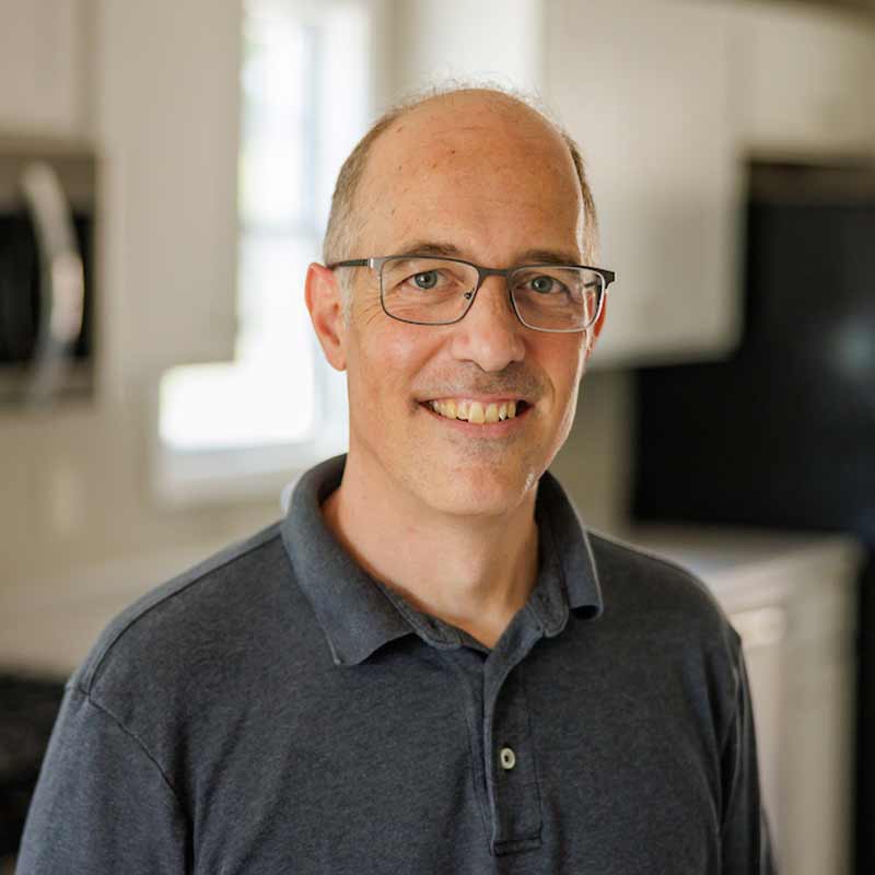 A headshot of John Mellor, a man wearing glasses and a dark gray polo shirt.