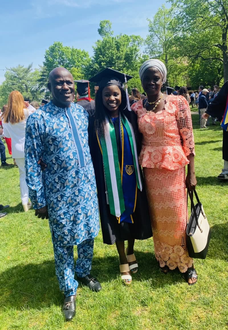 Godiya standing with her parents wearing a cap and gown after graduation ceremonies.