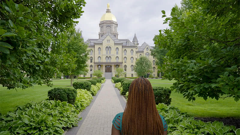 Godiya walking towards the main building with the dome in frame.