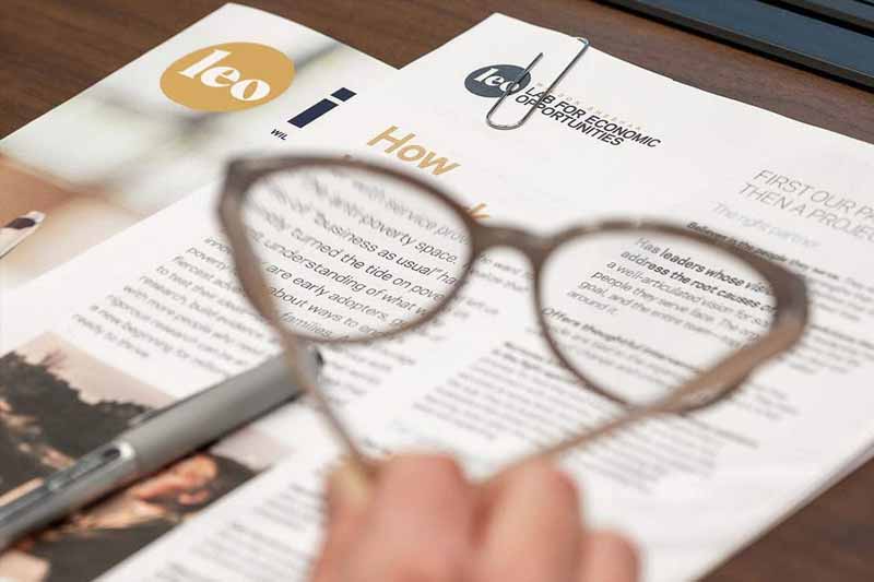 Papers and booklets on a desk and glasses in blurred in the foreground.