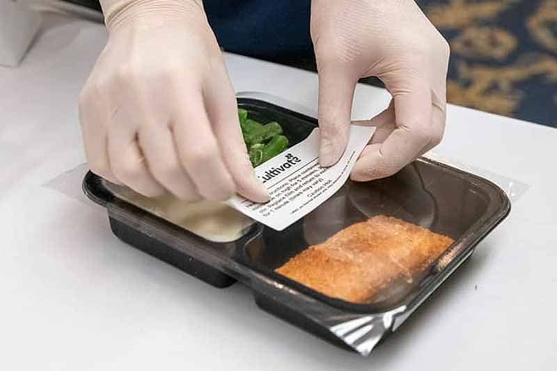 Gloved hands place a sticker on a frozen meal.