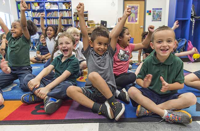 A group of young, excited children sitting on a colorful carpet