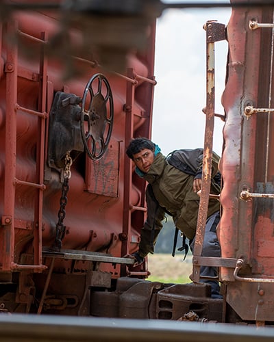 A man riding a train in motion looking off frame in a seemingly perilous situation.