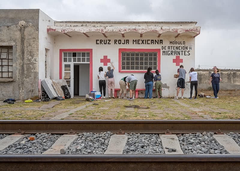 Students painting a red cross station with paintbrushes in hand.